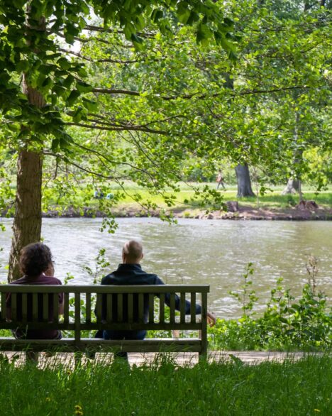 2 women sitting on bench near body of water during daytime