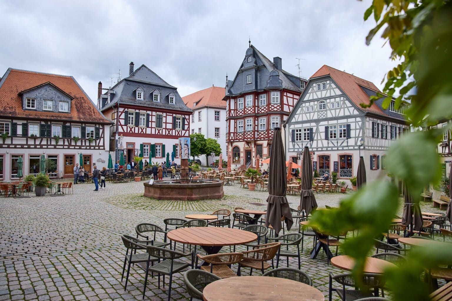 IDEE Living - Ein kopfsteingepflasterter Stadtplatz mit Sitzgelegenheiten im Freien, umgeben von Fachwerkhäusern mit roten und schwarzen Details.