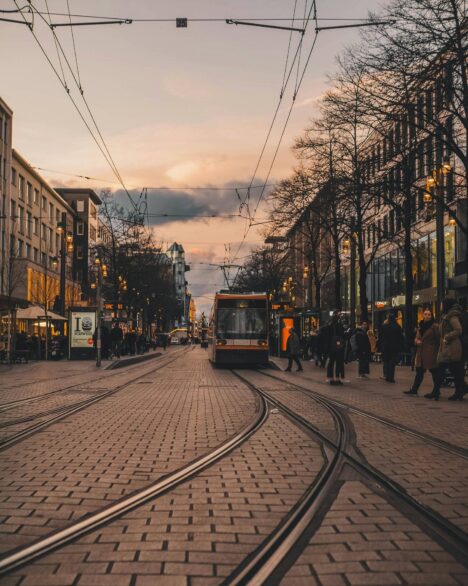 Modern tram on railroad with people walking in old town with low rise buildings in cold twilight