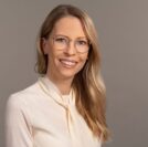 image0 IDEE Living - Eine Frau mit Brille und weißem Hemd in ihrer Wohnung.