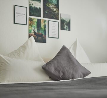 IDEE Living - Ein Bett mit Kissen und Bildern darüber.